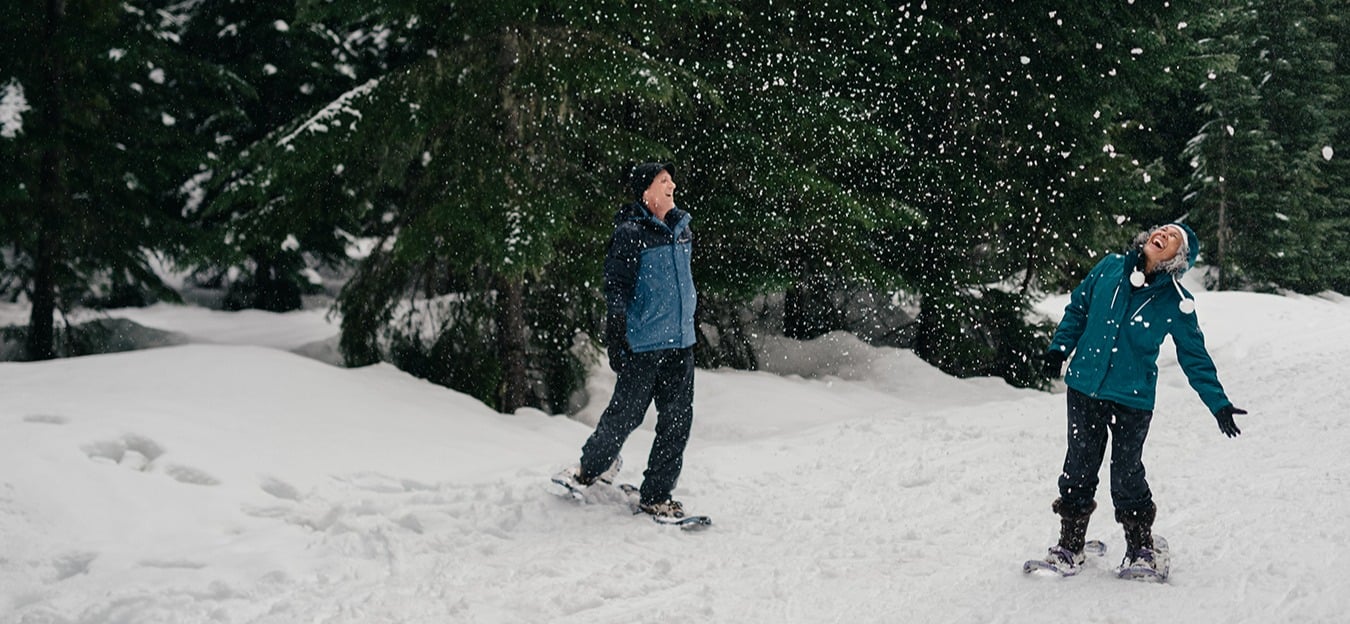 middle aged couple snow shoeing in the woods surrounded by pine trees